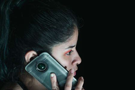 close-up of a beautiful latina woman with green hair receiving a call, with her cell phone in her hand. her eyes are made up in red and she has a serious look in her eyes. technology conceptの写真素材