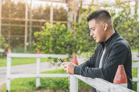 entrepreneur next to the wooden fence with his cell phone in his hands looking at his business accounts, a university student happy for his achievements, with a beautiful sunset in the background.の写真素材