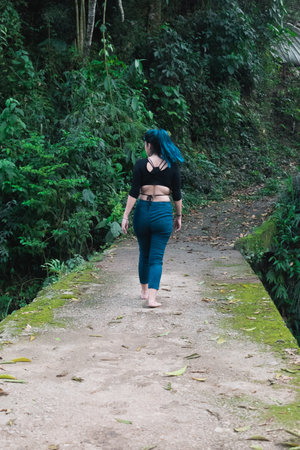 young latina woman with blue hair, walking on a cement bridge without railings covered with moss, in the middle of the humid Colombian jungles. girl hiking with bare feet.の写真素材