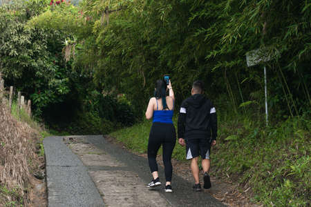 young latin couple out for a walk on a cold morning in the beautiful colombian trails, surrounded by green nature. young influencers recording content for their social networks.の写真素材
