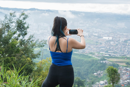 influencer girl creating content for her social networks, while hiking. latina woman on top of a mountain taking a picture with her two hands on her mobile phone. technological conceptの写真素材