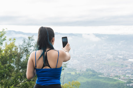 girl influencer creating content for her social networks, while hiking. concept of technology. latina woman hiking on a cold day to take pictures of the beautiful scenery.の写真素材