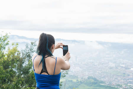 influencer girl creating content for her social networks, while hiking. latina woman at the top of a mountain recording a video and stabilizing the mobile phone with her hands. technological conceptの写真素材