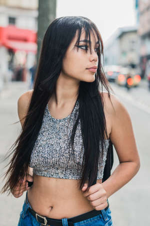 beautiful brown-skinned latina girl walking down the street in the city of Pereira-Colombia. young university student walking distractedly with her hands clutching the straps of her purse.の写真素材