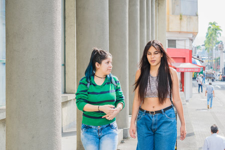two beautiful latina girls (caucasian and brunette) walking down the street. woman explaining to her friend about reports and jobs. girl with a disgusted expression on her face.の写真素材