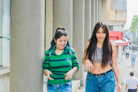 two beautiful latina girls (caucasian and brunette) walking down the street very cheerful while talking and discussing their dreams and future goals. two smiling women taking a stroll through the cityの写真素材
