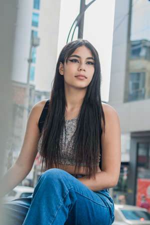 beautiful latina woman with brown skin, sitting on the sidewalk in the streets of the city of Pereira-Colombia. student girl thinking about her future and life project. educational concept.の写真素材