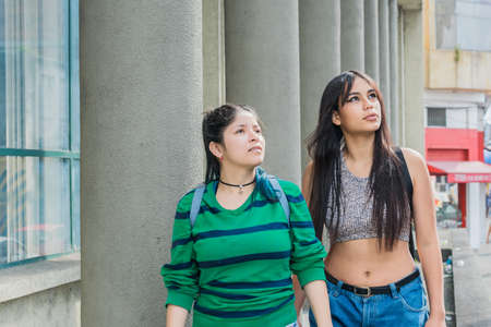 two beautiful latina girls (caucasian and brunette) walking down the street very happy while talking...