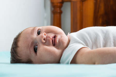beautiful baby latina with an angry expression on her face as she looks to her right, lying on a bed with a wooden backrest and wearing a white jumpsuit.の写真素材