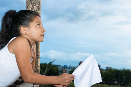 beautiful latina girl, brunette with her eyes raised looking up to the sky with a lot of illusion in her face, with a white flag in her hand (peace flag) thinking about her freedom. concept of freedomの写真素材