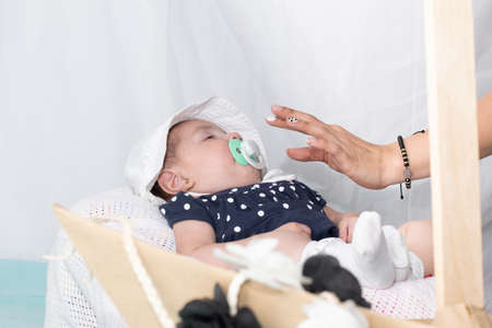 Hand of a mother putting a pacifier on her four month old baby to help her fall asleep. beautiful latin baby sleeping in her crib with a white hat. concept of motherhoodの写真素材