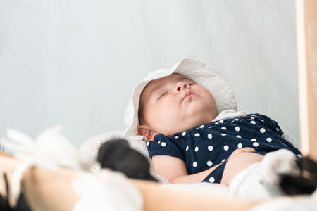 beautiful four month old latina baby girl sleeping peacefully in her room, with her face up and dressed in a blue romper suit and a white hat. 
concept of tenderness.の写真素材