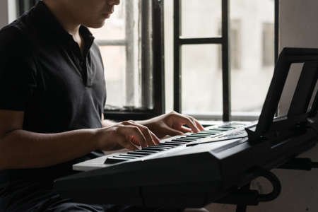 young latin male playing the electric piano or synthesizer. very focused on his hobbies creating new melodies and sounds. boy studying music production through virtual platforms.の写真素材