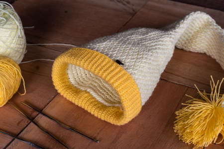 beautiful winter hat design made by a colombian artisan. elf hat knitted with crochet technique, placed on a wooden board with rolls of wool and needles on its side.の写真素材