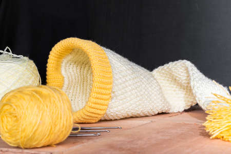 baby elf cap crocheted on wooden boards and a black background, next to it two rolls of yellow and...