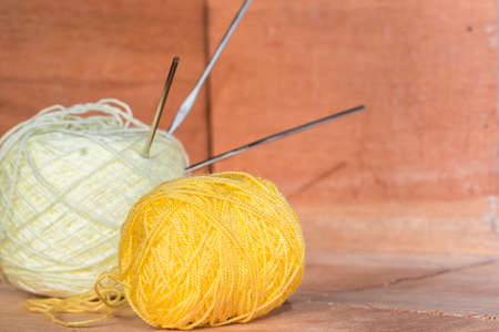 two rolls of yellow and white yarn to crochet, with needles stuck on them, on an orange wooden background. yarn ready to start crocheting at home. concept of home workの写真素材