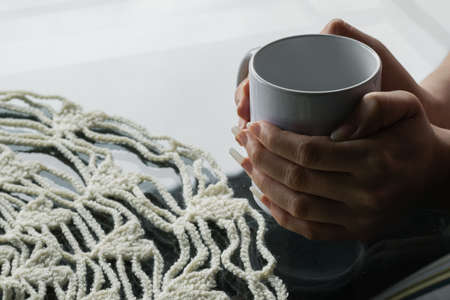 latina woman's hands holding a white cup with coffee, hugging the cup to warm her hands from the...