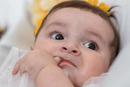 beautiful latina baby bored, lying in her crib, while looking at her surroundings. six month old baby girl touching her gums with her thumb.の写真素材