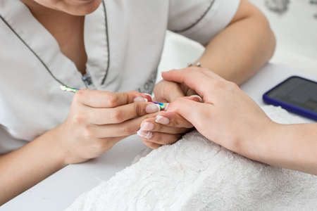 latina manicurist working at home, cleaning a girl's nails with the cuticle pusher. woman learning the art of manicuring, painting and decorating nails.の写真素材