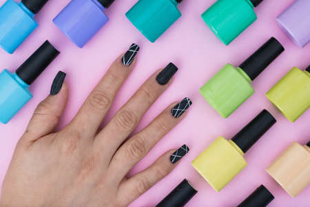 top view of a girl's hand with nails painted black with white. pattern of enamels of different colors placed on a pink, purple, blue, green and yellow background. elements to make a nail paintingの写真素材