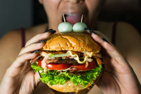 latina girl about to bite a hamburger she is holding with both hands. hamburger with two quail eggs...