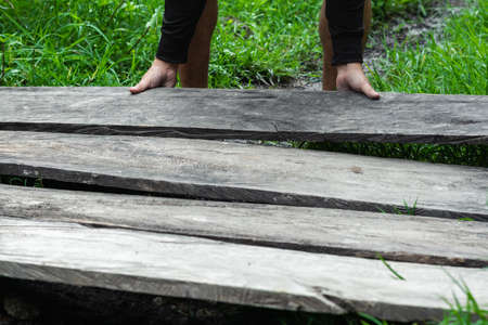 young latin guy laying some old gray wooden planks on a grassy land, construction of a wooden path or floor. concept of prosperity. scarce economic resources in a popular neighborhoodの写真素材