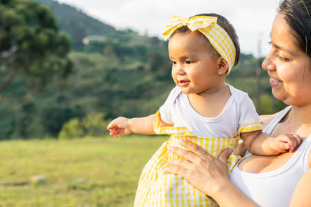 latin mother holding her daughter in an outdoor field, smiling and living a beautiful family moment. summer day with mom. concept of joy.の写真素材