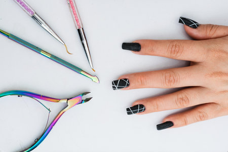 hand of a girl with her nails made in polygel on a white background and next to her the ideal elements for a basic manicure. cuticle nippers, cuticle pusher and fine painting and design brushesの写真素材