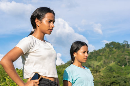 two indigenous latina girls from the Escopetera and Pirza indigenous reservation, standing on a mountaintop looking into the distance, in the background a blue skyの写真素材