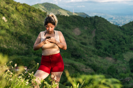 beautiful young latina woman, on top of a hill using her cell phone to communicate. in the...