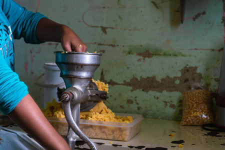 young latina girl with brown skin, grinding cooked corn in a corn grinding machine, pushing the corn through the hopper part to compress and finish fasterの写真素材