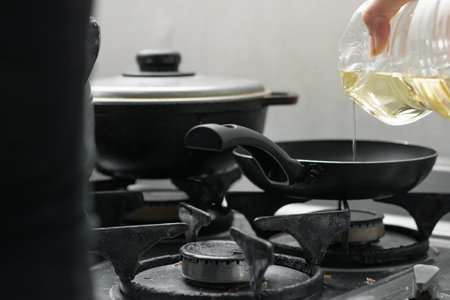 girl pouring the oil into the frying pan, which is on top of a burner, on a gas stove, preparing the typical Colombian breakfast.の写真素材