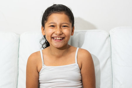 portrait of latin brunette girl, sitting on the sofa smiling and showing her teeth, girl with indian featuresの写真素材
