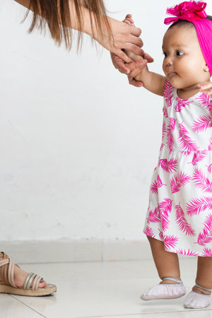 baby brunette holding her mother's arm to keep from falling. learning to take her first steps.