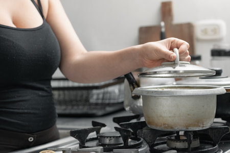 young woman uncovering a pot on the gas stove, lifting the lid to see the food she is preparing.の写真素材