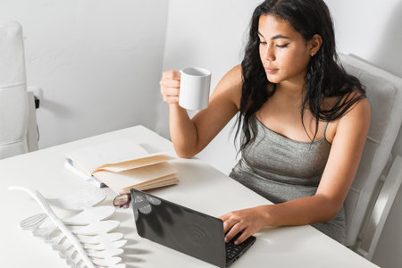 dark-skinned latina girl surfing on her laptop while drinking a cup of coffee. woman studying quietly.の写真素材
