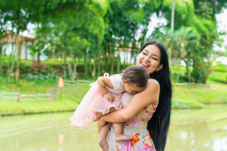 latina woman holding her baby with a big smile, little girl bending her head to look for her mother's breast to feed from her milk. concept of motherhoodの写真素材