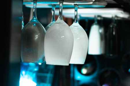 white wine glasses hanging over the top, in a liquor cabinet in a bar, with an ambiance of blue light on a black background.の写真素材