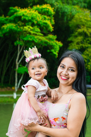 portrait of a mother and daughter smiling happily as they stroll through a green park surrounded by trees.の写真素材