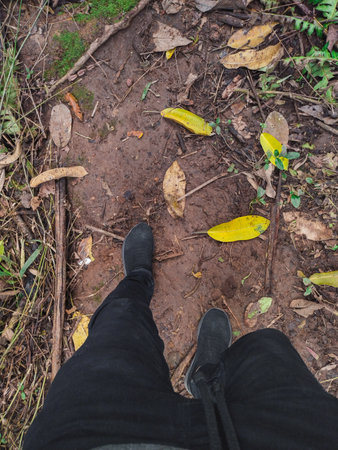 view of a man's feet hiking on a dirt road, man in black trousers walking on a dirt road