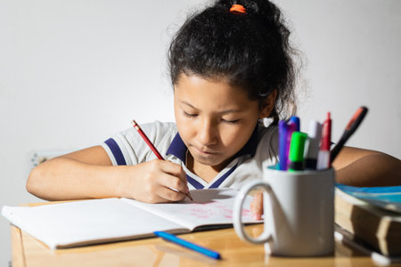 little girl, Latina student doing her homework very concentrated, working on top of her wooden desk.の写真素材