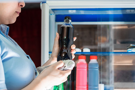 detailed view of a girl carefully cleaning a soda bottle while working in a store.の写真素材