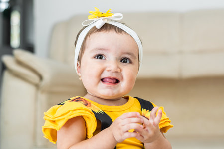 beautiful latina baby, very happy, smiling and showing her tongue, she is wearing a yellow dressの写真素材