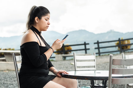 young latina woman, looking at her cell phone, while sitting in an outdoor cafÃ©の写真素材