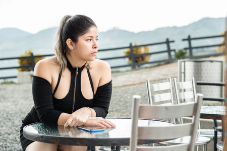 young latina woman, sitting waiting for the food she ordered, in an open-air restaurantの写真素材