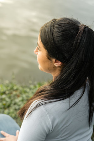 view from above of a young latin woman sitting by a lake, admiring the sunsetの写真素材
