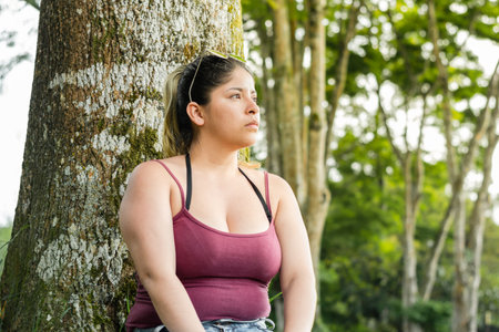 young latina woman, sitting next to a tree in a park, looking and meditatingの写真素材
