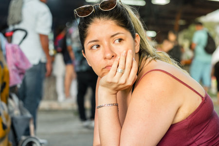 young latin woman waiting sitting on the street, with her hand on her face with a bored expressionの写真素材
