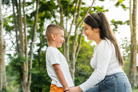 young latina mother, on her knees proudly looking at her young son, while playing in a park.の写真素材