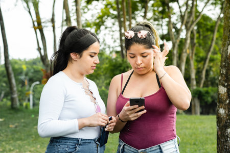 two latina friends worried about what they are looking at on their cell phones. concept of bad newsの写真素材